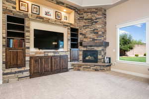 Living room featuring an outdoor stone fireplace, carpet floors, and built in features