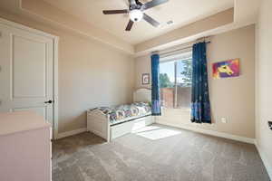 Bedroom featuring a tray ceiling, light carpet, and a ceiling fan