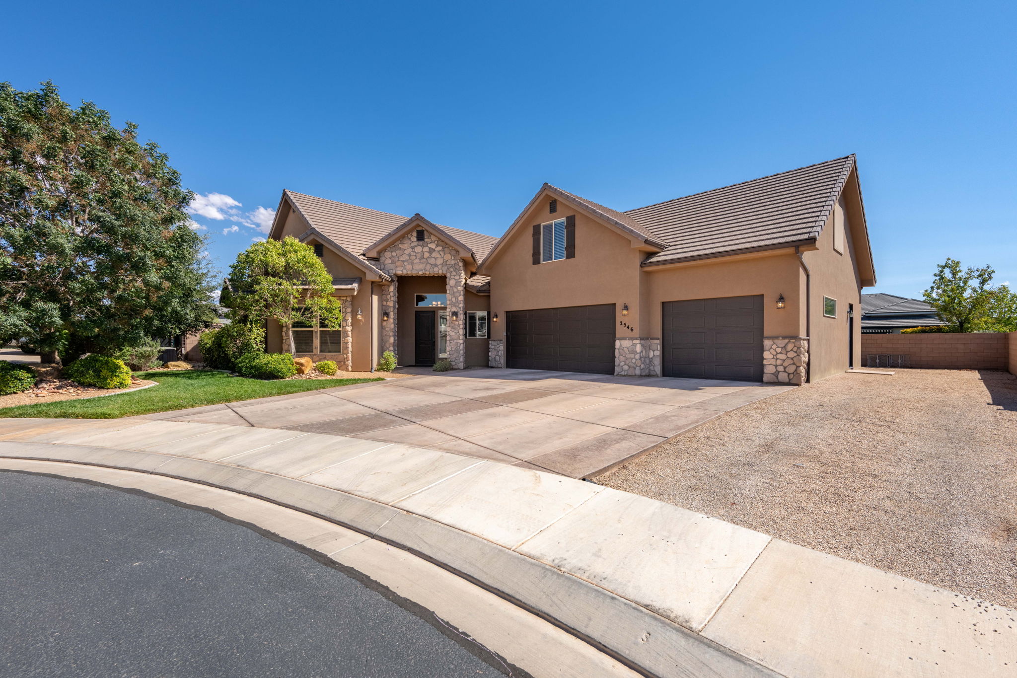 View of front of house with stone siding, concrete driveway, stucco siding, a tile roof, and an attached garage