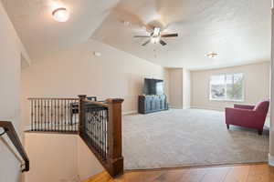 Living area with light wood finished floors, a textured ceiling, lofted ceiling, a ceiling fan, and light colored carpet