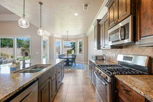 Kitchen with stainless steel appliances, decorative light fixtures, crown molding, a textured ceiling, and light tile patterned floors
