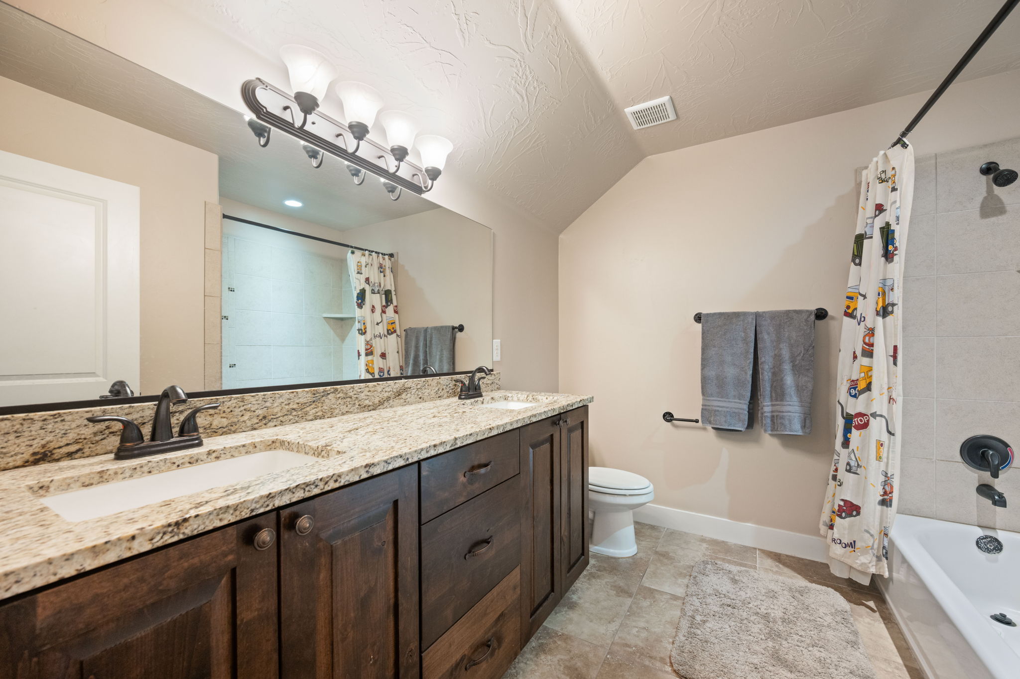 Bathroom featuring shower / tub combo, double vanity, vaulted ceiling, and a textured ceiling