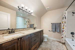Bathroom featuring shower / tub combo, double vanity, vaulted ceiling, and a textured ceiling