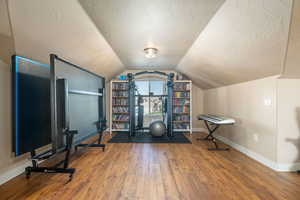 Workout room with vaulted ceiling, a textured ceiling, and wood finished floors