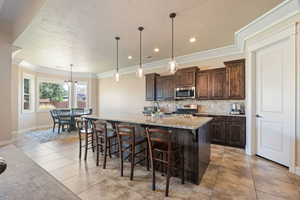 Kitchen featuring dark brown cabinetry, a kitchen breakfast bar, decorative backsplash, hanging light fixtures, and light stone counters