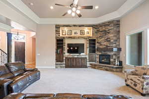 Carpeted living area featuring ceiling fan, a fireplace, stairs, built in shelves, and a chandelier