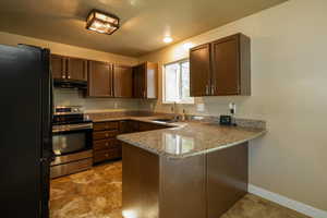 Kitchen featuring freestanding refrigerator, stainless steel electric range oven, a peninsula, dark brown cabinetry, and light stone counters