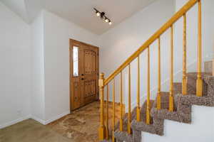 Foyer with stairway, light colored carpet, and rail lighting