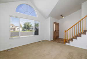 Foyer featuring carpet, stairs, and high vaulted ceiling