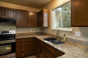 Kitchen with electric stove, ventilation hood, dark brown cabinets, light stone countertops, and a textured ceiling