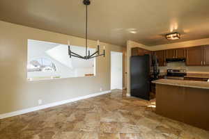 Kitchen featuring freestanding refrigerator, stainless steel electric range, a chandelier, light stone counters, and decorative light fixtures