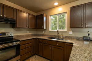 Kitchen featuring stainless steel range with electric stovetop, extractor fan, dark brown cabinetry, a textured ceiling, and light stone countertops