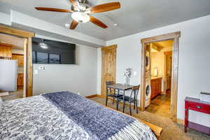Bedroom featuring ensuite bath, freestanding refrigerator, a textured ceiling, a ceiling fan, and stacked washer / dryer