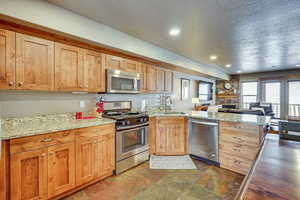 Kitchen featuring appliances with stainless steel finishes, a peninsula, light stone counters, open floor plan, and dark stone finish flooring