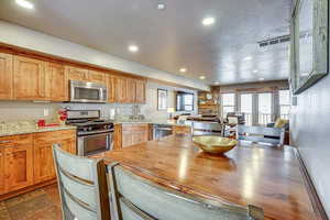 Kitchen featuring stainless steel appliances, light stone countertops, recessed lighting, a peninsula, and brown cabinetry
