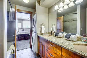Ensuite bathroom with double vanity, estacked washer and dryer, a textured ceiling, ceiling fan, and shower / tub combo