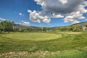 View of community with view of golf course, a water and mountain view, and a lawn