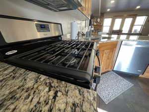 Kitchen with stainless steel appliances, brown cabinets, light stone countertops, and stone tile floors
