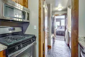2nd Kitchen with stainless steel appliances, brown cabinetry, stone tile floors, and light stone countertops