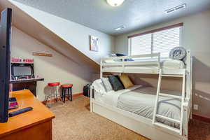 Bedroom featuring light colored carpet, a textured ceiling, and a desk