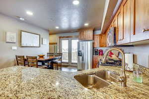 Kitchen featuring appliances with stainless steel finishes, brown cabinets, a textured ceiling, light stone countertops, and recessed lighting