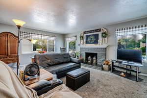 Carpeted living area with a textured ceiling, healthy amount of natural light, and a brick fireplace
