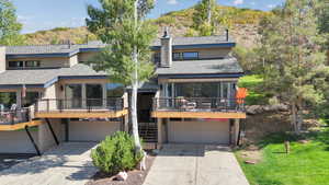 View of front of property featuring a wooden deck, driveway, a garage, and roof with shingles