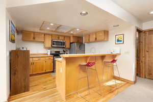 Kitchen with a kitchen breakfast bar, appliances with stainless steel finishes, a peninsula, light wood finished floors, and recessed lighting