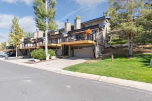 Back of property featuring a lawn, a wooden deck, concrete driveway, a garage, and stairs