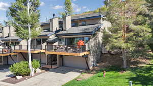 Rear view of house with a chimney, a wooden deck, a shingled roof, driveway, and an attached garage
