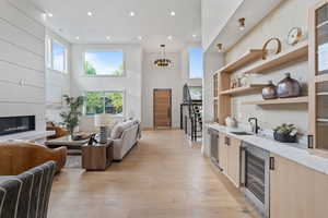 Indoor wet bar featuring light wood-style floors, recessed lighting, a towering ceiling, wine cooler, and pendant lighting