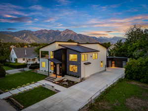 Contemporary house with concrete driveway, a mountain view, a metal roof, and a front lawn