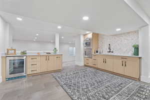 Bar area with light brown cabinets, wine cooler, recessed lighting, stainless steel double oven, and light stone countertops