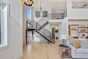 Living room with light wood-style floors, a towering ceiling, stairway, recessed lighting, and beverage cooler