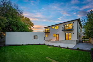 Back of property at dusk featuring a patio area, a balcony, a yard, and stucco siding