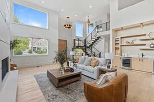 Living room with a towering ceiling, light wood-type flooring, recessed lighting, beverage cooler, and a glass covered fireplace