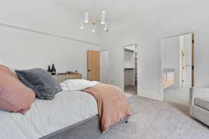 Bedroom featuring a high ceiling, a walk in closet, light colored carpet, a chandelier, and ensuite bathroom