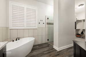 Full bathroom with vanity, a freestanding tub, dark wood-type flooring, a shower stall, and a walk in closet