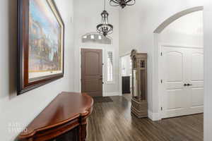 Foyer entrance with dark wood finished floors, a chandelier, a towering ceiling, and arched walkways