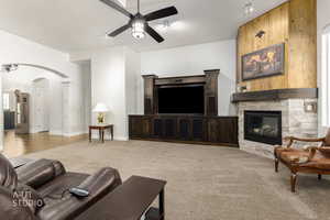 Living area featuring arched walkways, ceiling fan, light carpet, a fireplace, and a textured ceiling