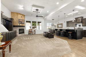 Living room with a textured ceiling, ceiling fan, a stone fireplace, and light wood finished floors