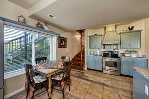 Kitchen with stainless steel range with electric stovetop, light tile patterned floors, and custom range hood