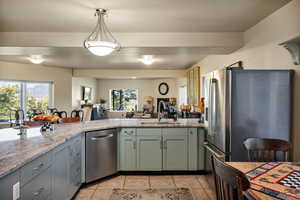 Kitchen featuring light stone countertops, open floor plan, stainless steel appliances, light tile patterned floors, and pendant lighting