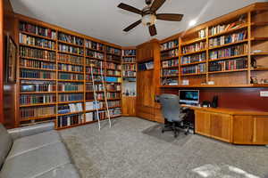 Office featuring wall of books, light carpet, and ceiling fan
