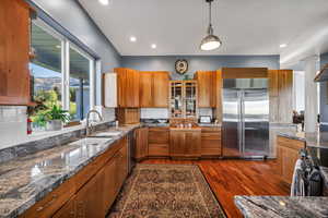 Kitchen with appliances with stainless steel finishes, brown cabinetry, decorative backsplash, granite countertops, and recessed lighting