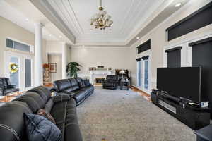 Carpeted living area with ornamental molding, a glass covered fireplace, a tray ceiling, recessed lighting, and a chandelier