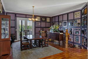 Dining space featuring a decorative wall, crown molding, dark wood-style flooring, and a chandelier