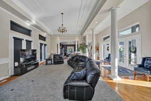 Living room featuring ornate columns, wood finished floors, french doors, crown molding, and a raised ceiling