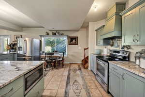Kitchen featuring light tile patterned floors, appliances with stainless steel finishes, green cabinetry, gray cabinets, and light stone countertops