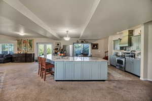 Kitchen featuring beam ceiling, light colored carpet, appliances with stainless steel finishes, a kitchen bar, and hanging light fixtures
